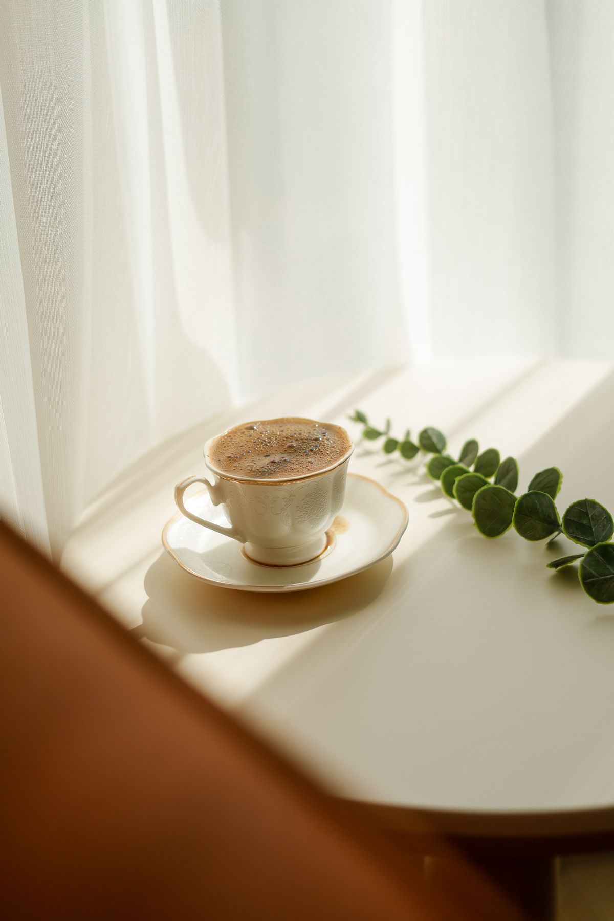 An elegant coffee cup on a sunlit table with greenery, evoking a slow morning